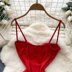 Red strappy top on a wooden hanger against a white textured background