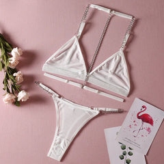 White bikini set with chain details on a pink background with flowers and cards.