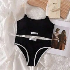 Black bikini set with 'Fashion' label on a textured surface with a magazine and wooden object.