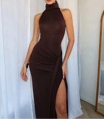 Woman wearing a brown high-neck dress with a slit, standing against a white curtain.