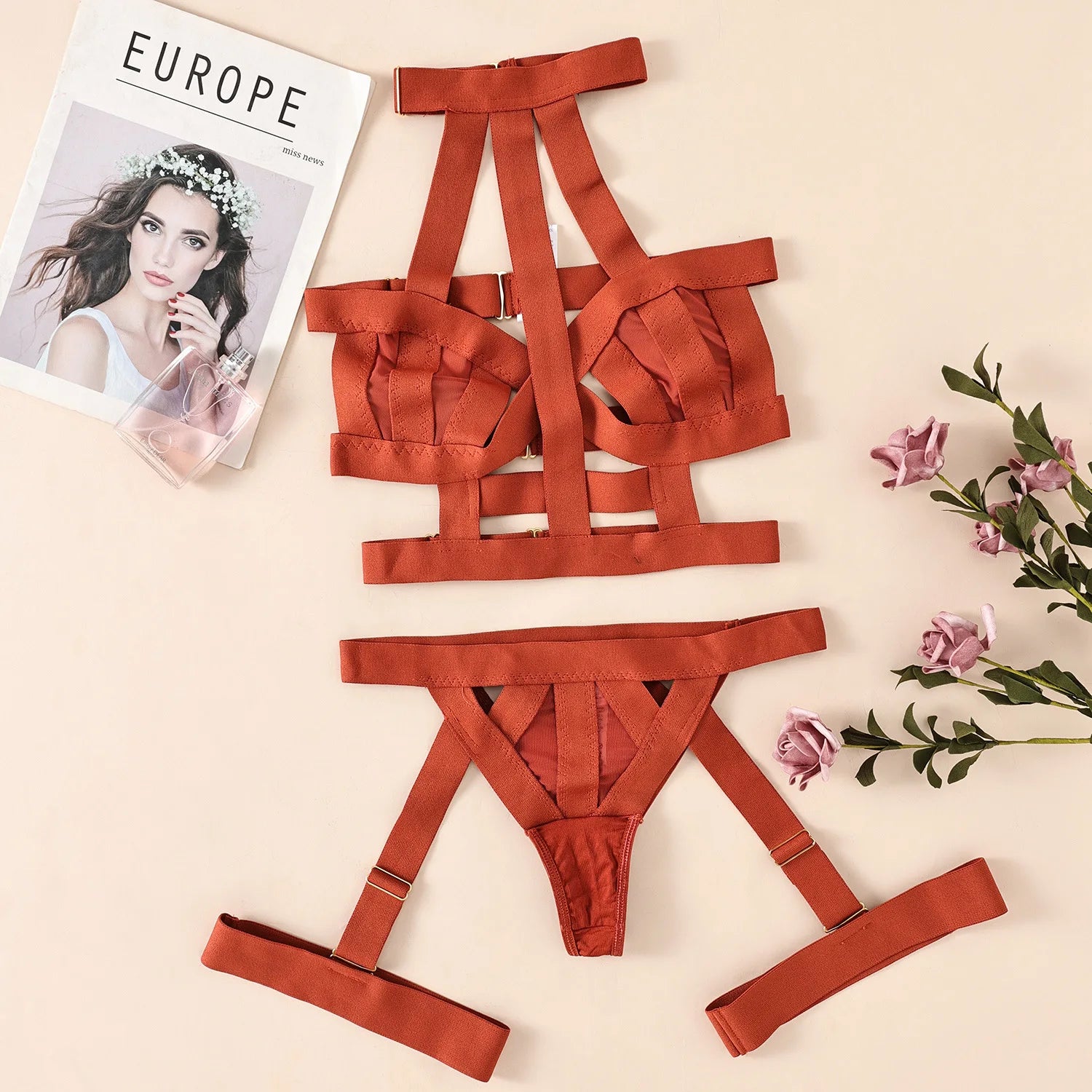 Red strappy lingerie set on a beige surface with flowers and a magazine.