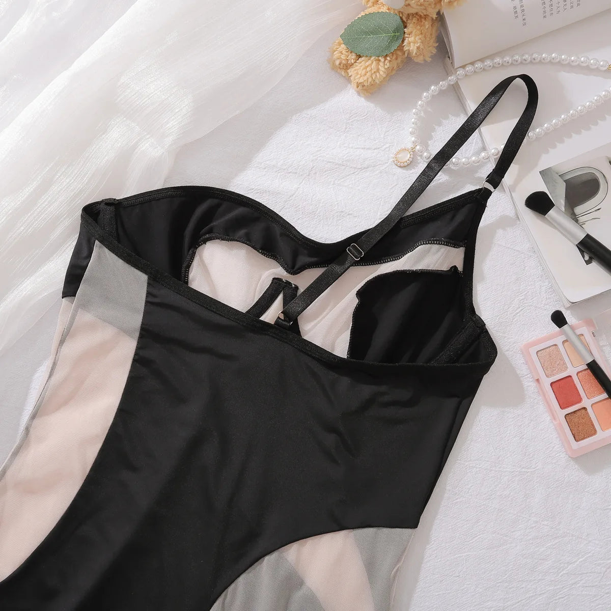 Black lingerie set on a white surface with makeup and a teddy bear.