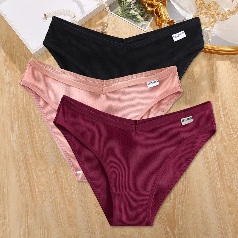 Three pairs of ribbed underwear in black, pink, and maroon on a wooden surface.