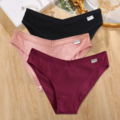 Three pairs of ribbed underwear in black, pink, and maroon on a wooden surface.