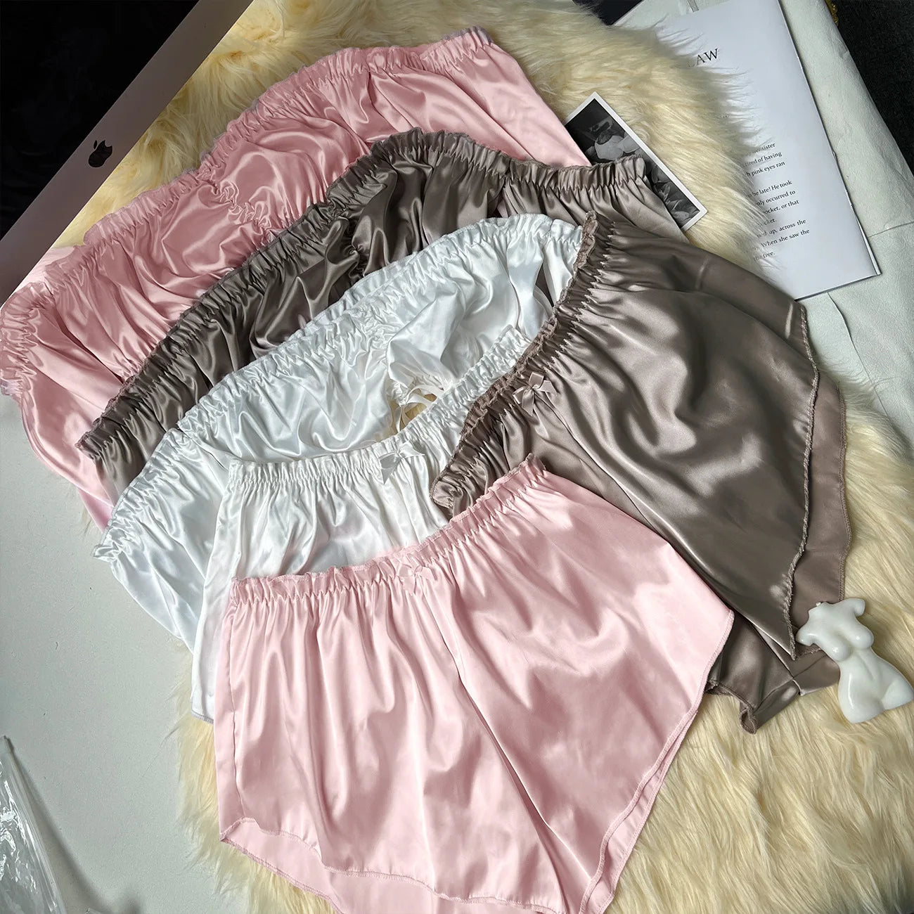Four pairs of satin shorts in pink, brown, and white on a fur surface.