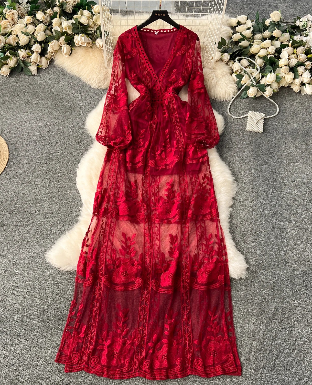 Red lace dress on a hanger with floral decorations on a gray surface