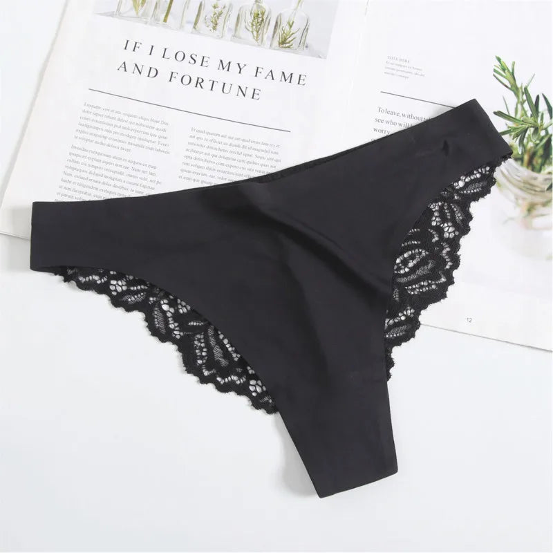 Black lace-trimmed underwear on a white surface with a magazine and plant in the background