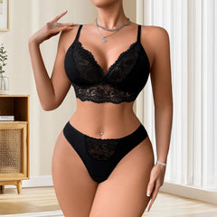 Woman wearing a black lace lingerie set in a room with a wooden cabinet and white curtains.