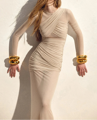 Woman wearing a beige dress with gold bracelets against a light background