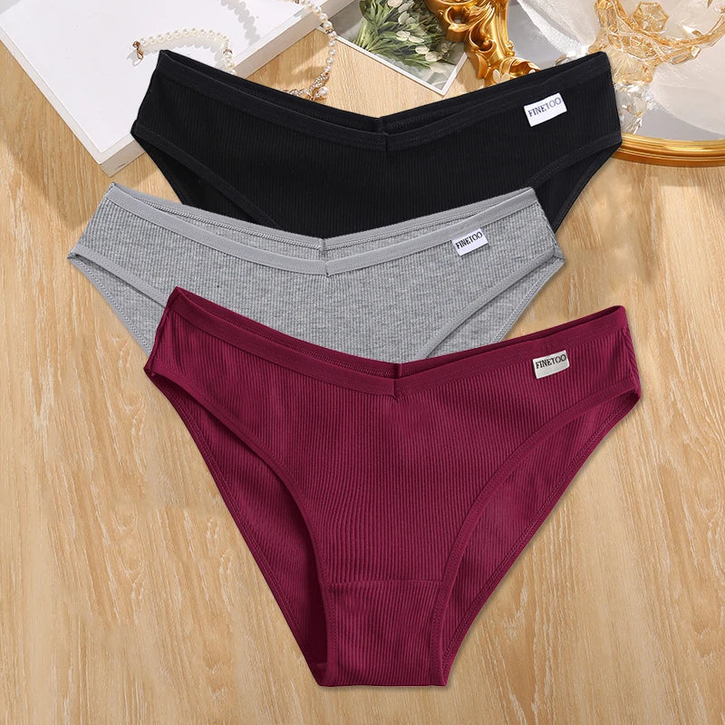 Three pairs of underwear in black, gray, and burgundy on a wooden surface.