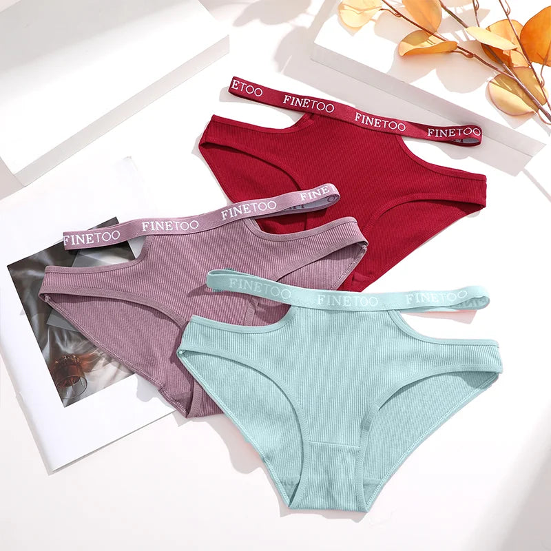 Three pairs of underwear in red, purple, and green with matching straps on a light background.