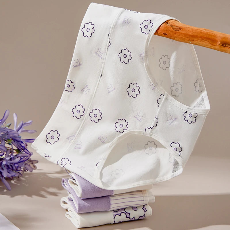 White baby bib with purple floral patterns on a wooden stand against a beige background.