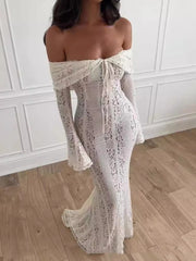 Woman wearing a white lace off-shoulder dress in a room with wooden flooring and white walls.