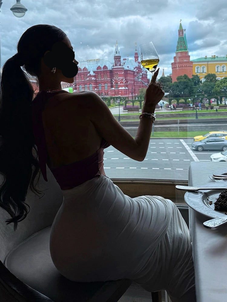 Woman in a white dress holding a glass of wine, with a cityscape in the background