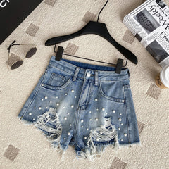 Denim shorts with pearl embellishments on a hanger with sunglasses, newspaper, and cup in the background.