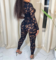 Woman wearing a black lace jumpsuit standing in a room with white curtains.