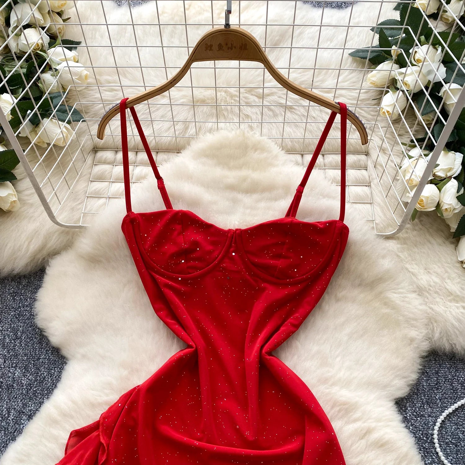 Red velvet dress on a hanger with a white fur rug and floral decorations in the background