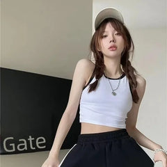 Person wearing a white tank top and black pants with a cap indoors.