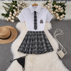 White shirt with black tie and plaid skirt on a fur surface with flowers and a hat.