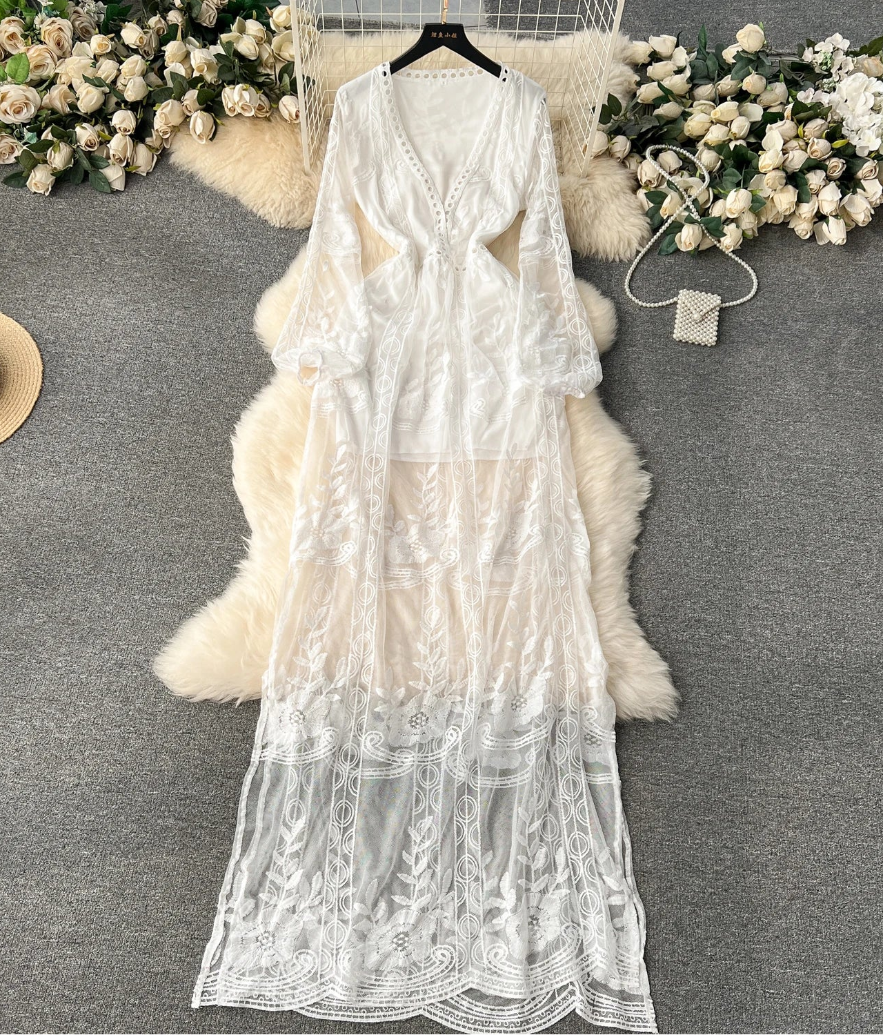 White lace dress on a hanger with decorative flowers and a hat on a gray surface
