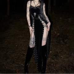 Person in a dark forest wearing a black dress with lace-up front and cross necklace.