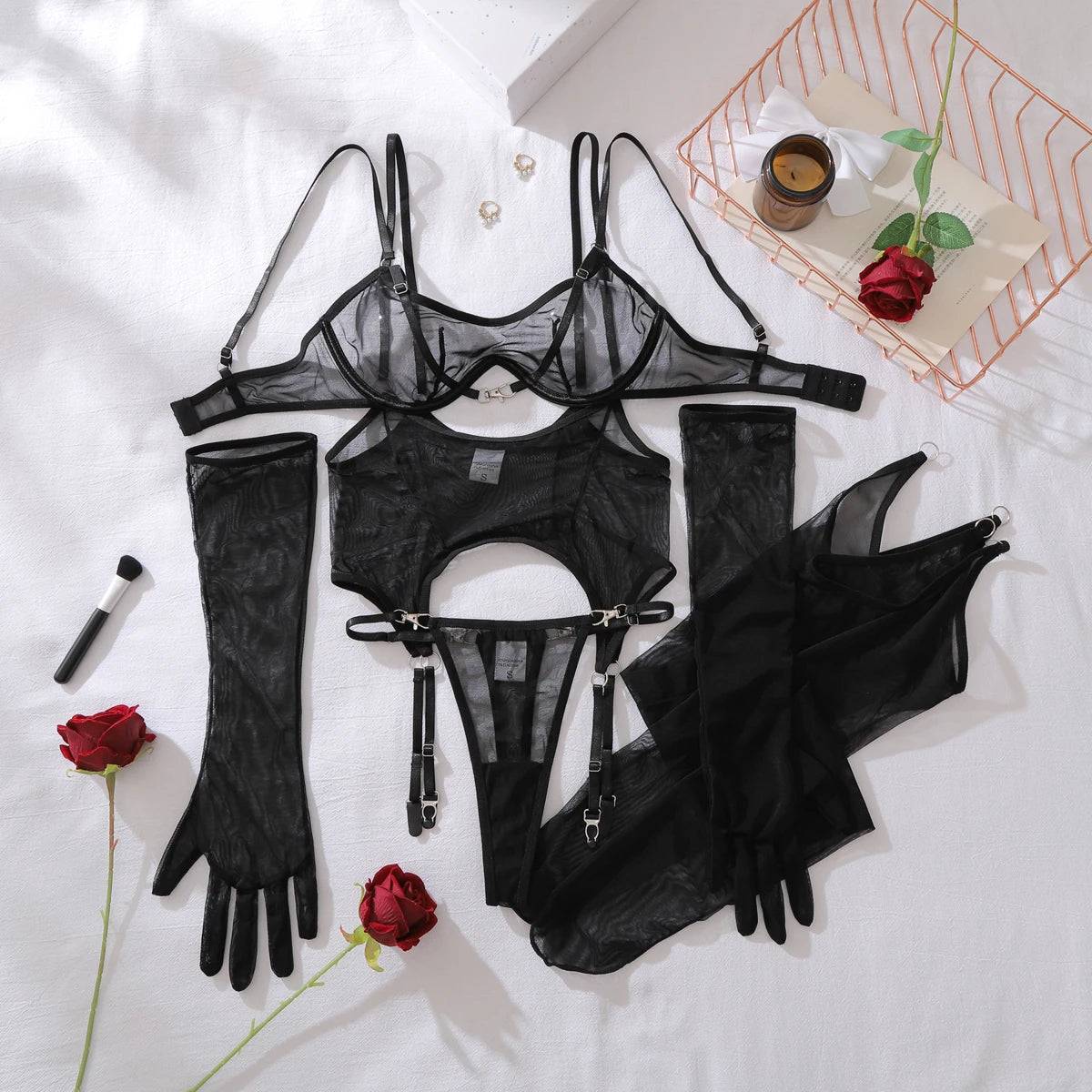 Black lingerie set with garter belt, bra, panties, and gloves on a white surface with red roses.