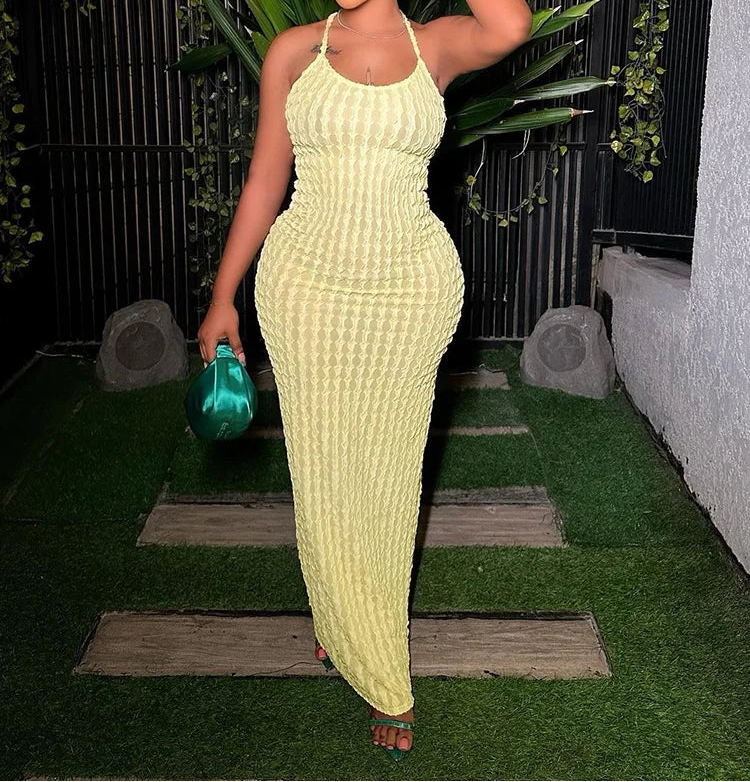 Woman in a light green dress standing outdoors with plants and a black metal fence in the background.