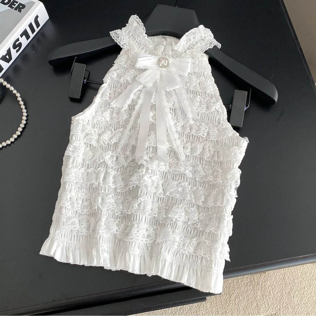 White lace dress on a black surface with a book and jewelry nearby