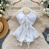 White dress with ruffled details on a hanger against a decorative background with flowers and a hat.