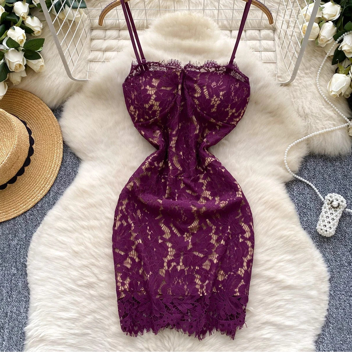 Purple lace dress on a hanger with decorative items on a fluffy white rug.