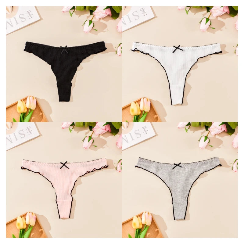 Four pairs of women's underwear in black, white, pink, and gray on a beige surface with flowers and cards.