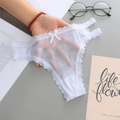 White lace-trimmed underwear held by a hand on a gray surface with glasses and a book.