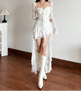 Woman wearing a white lace dress and boots in a room with wooden floor and white walls.