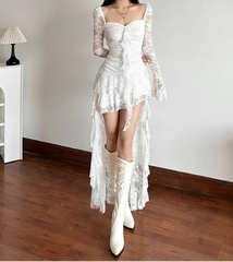 Woman wearing a white lace dress and boots in a room with wooden floor and white walls.