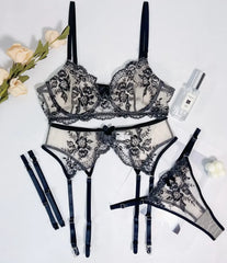 Black lace lingerie set with floral details on a white background, accompanied by a bottle of perfume and flowers.