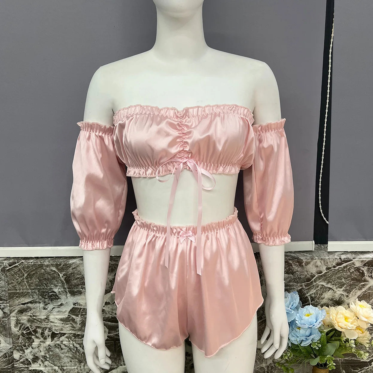 Mannequin wearing a pink satin outfit with matching top and shorts on a marble surface.