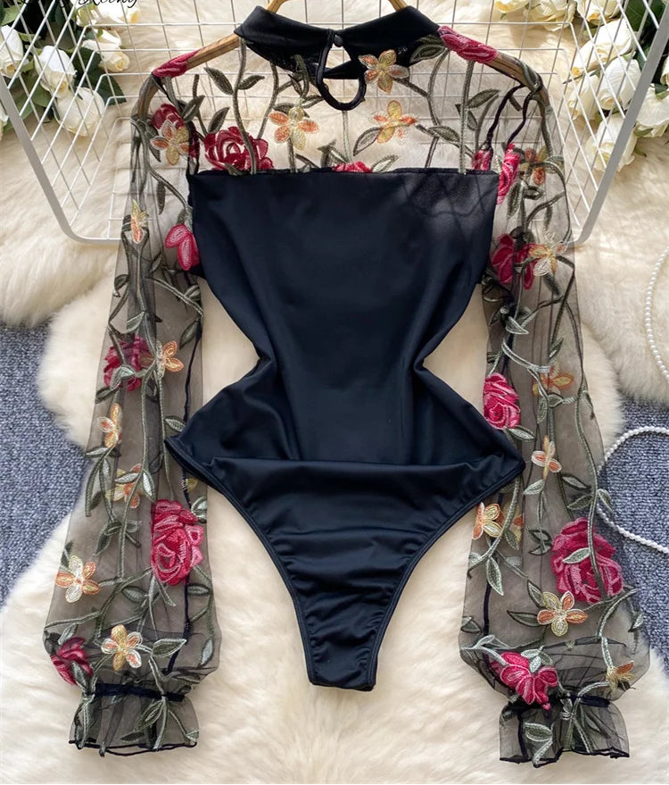 Black swimsuit with floral lace straps on a hanger against a white floral background
