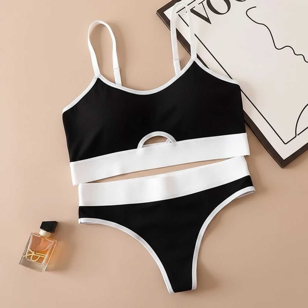 Black and white bikini set on a beige surface with a phone and perfume bottle.