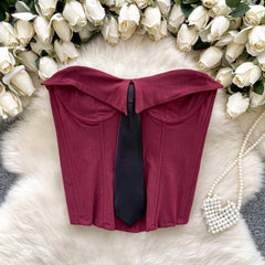 Red bandeau top with a black tie on a white fur surface with white flowers in the background