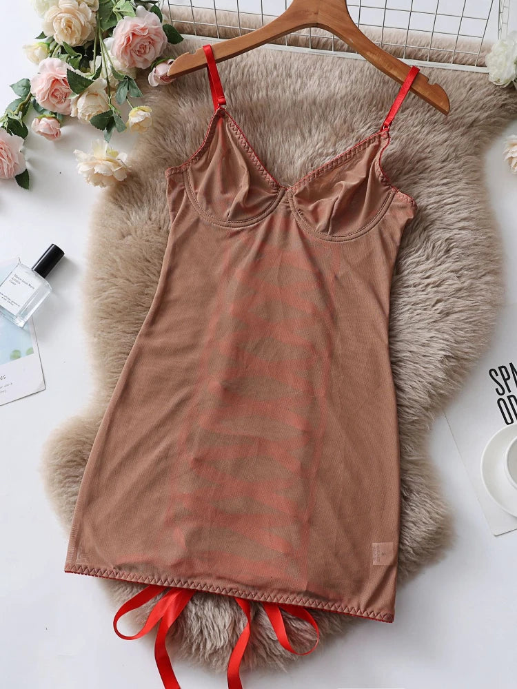 Brown slip dress with red straps on a hanger over a fluffy rug with flowers and a magazine in the background.
