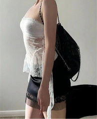 Person wearing a sheer white top and black shorts with a black bag on a plain background