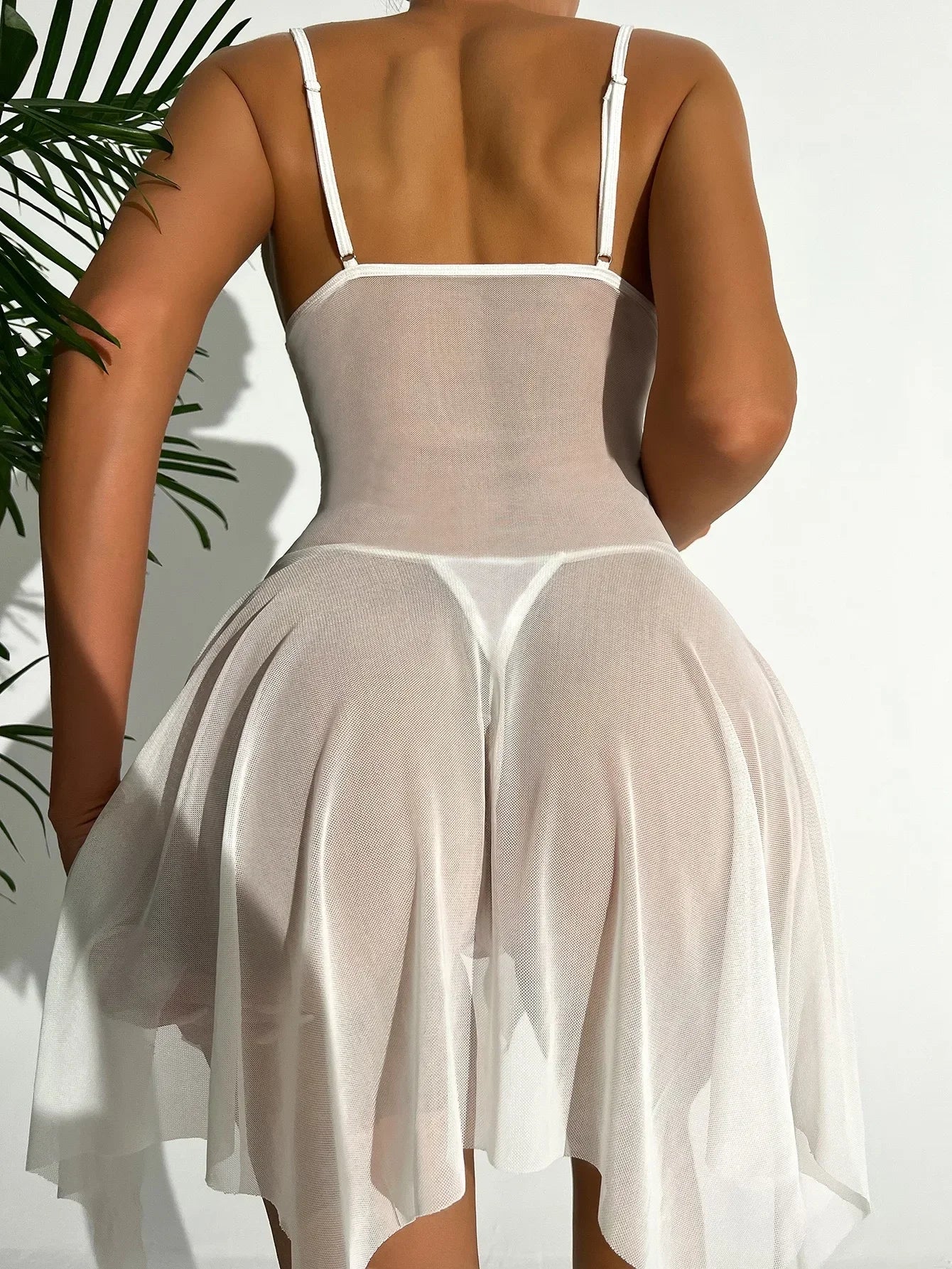 Woman wearing a sheer white dress with thin straps against a neutral background