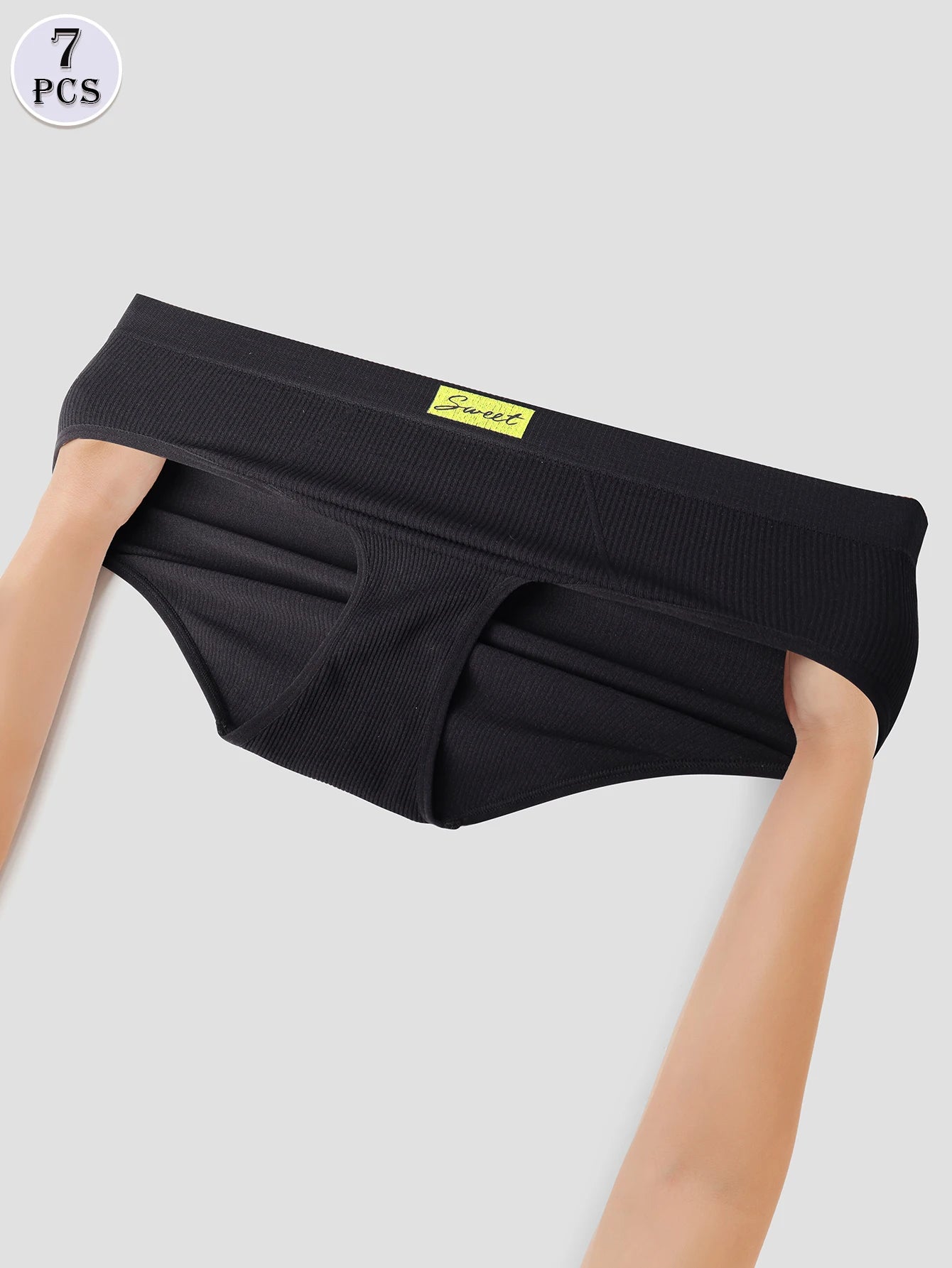 Black underwear held by a person on a light gray background