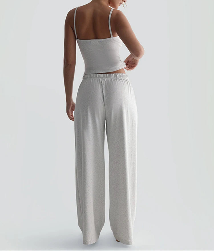 Woman wearing a white tank top and light gray wide-leg pants on a plain background