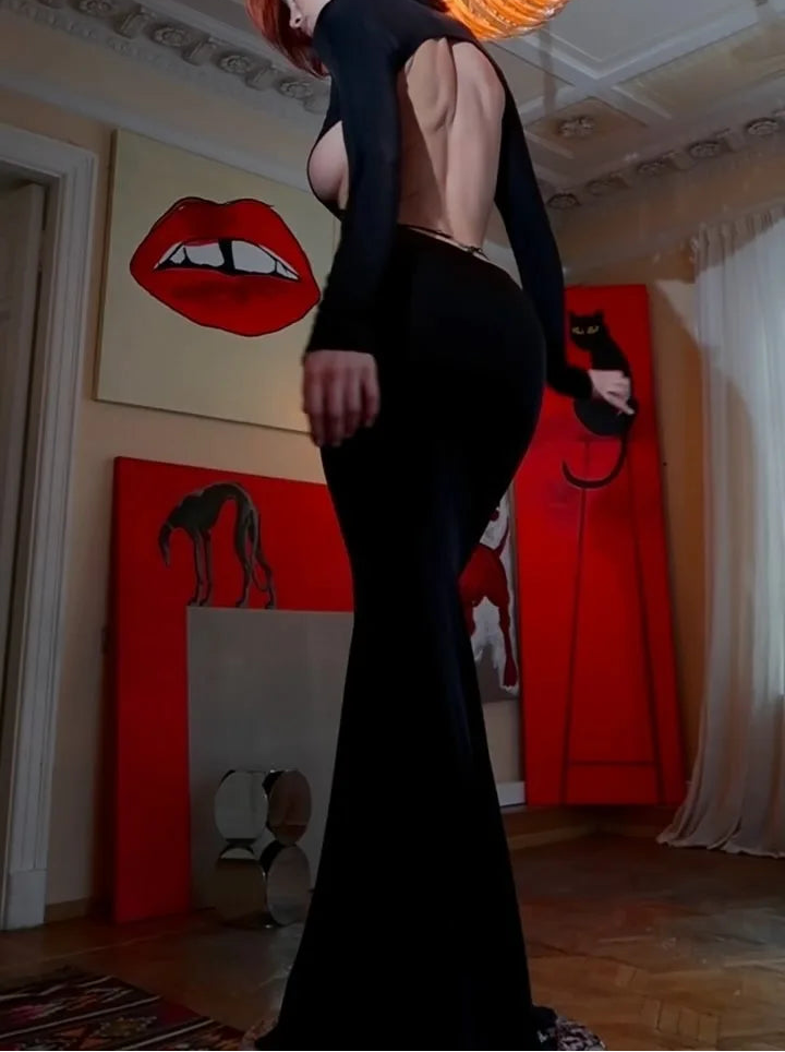 Woman in a black dress standing in a room with artistic wall decorations.