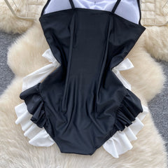 Black swimsuit with white ruffles on a textured surface