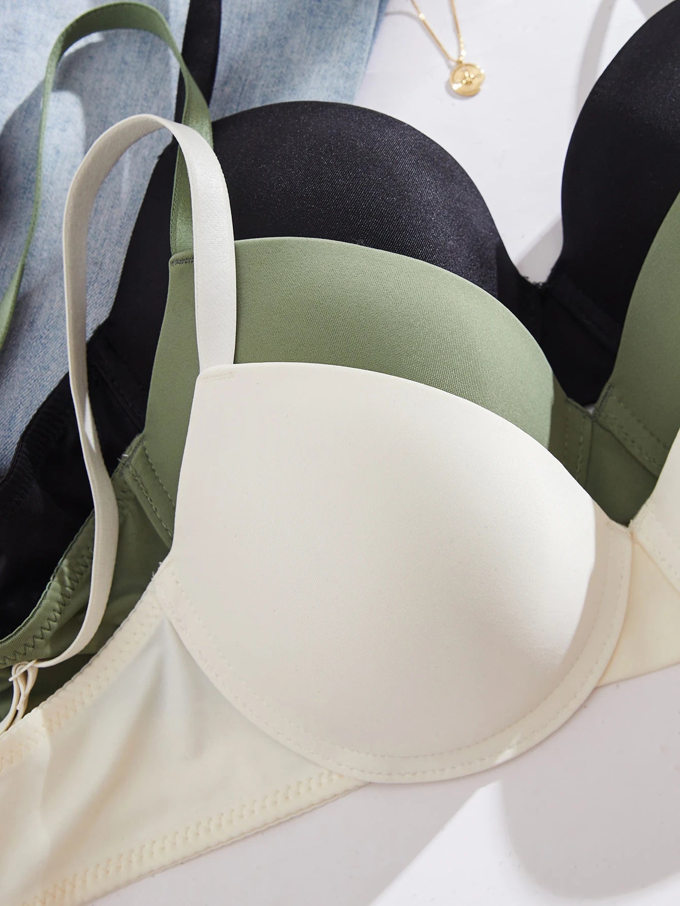 Three bras in black, green, and beige on a light gray background
