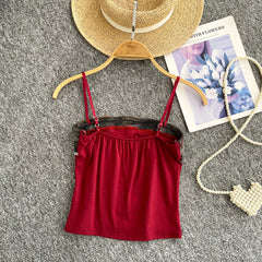 Red top on a hanger with a hat, newspaper, and pearl necklace on a gray surface