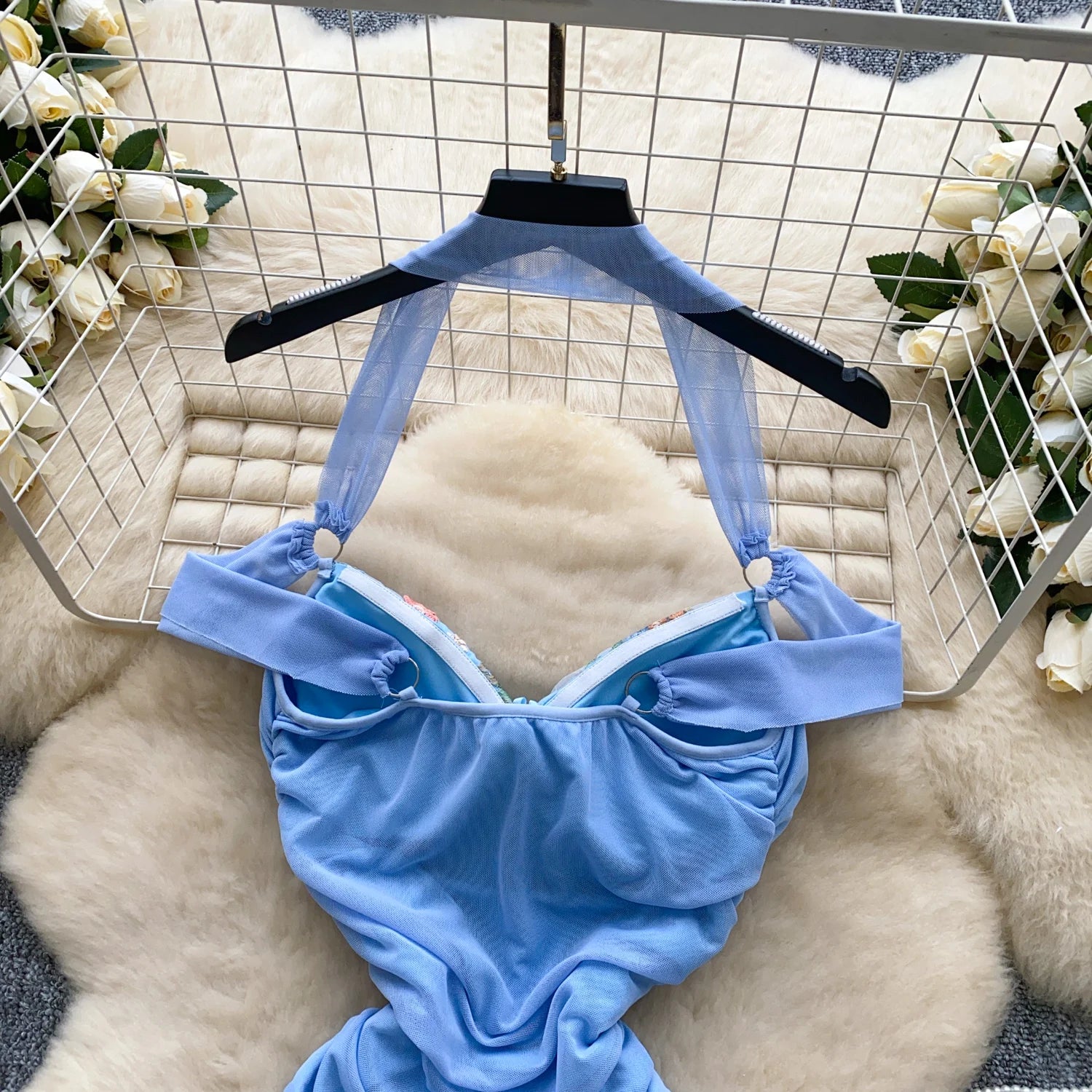 Blue swimsuit on a hanger against a decorative background with flowers and a basket.
