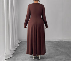 Woman wearing a brown long-sleeve dress standing in a room with white curtains and gray floor.